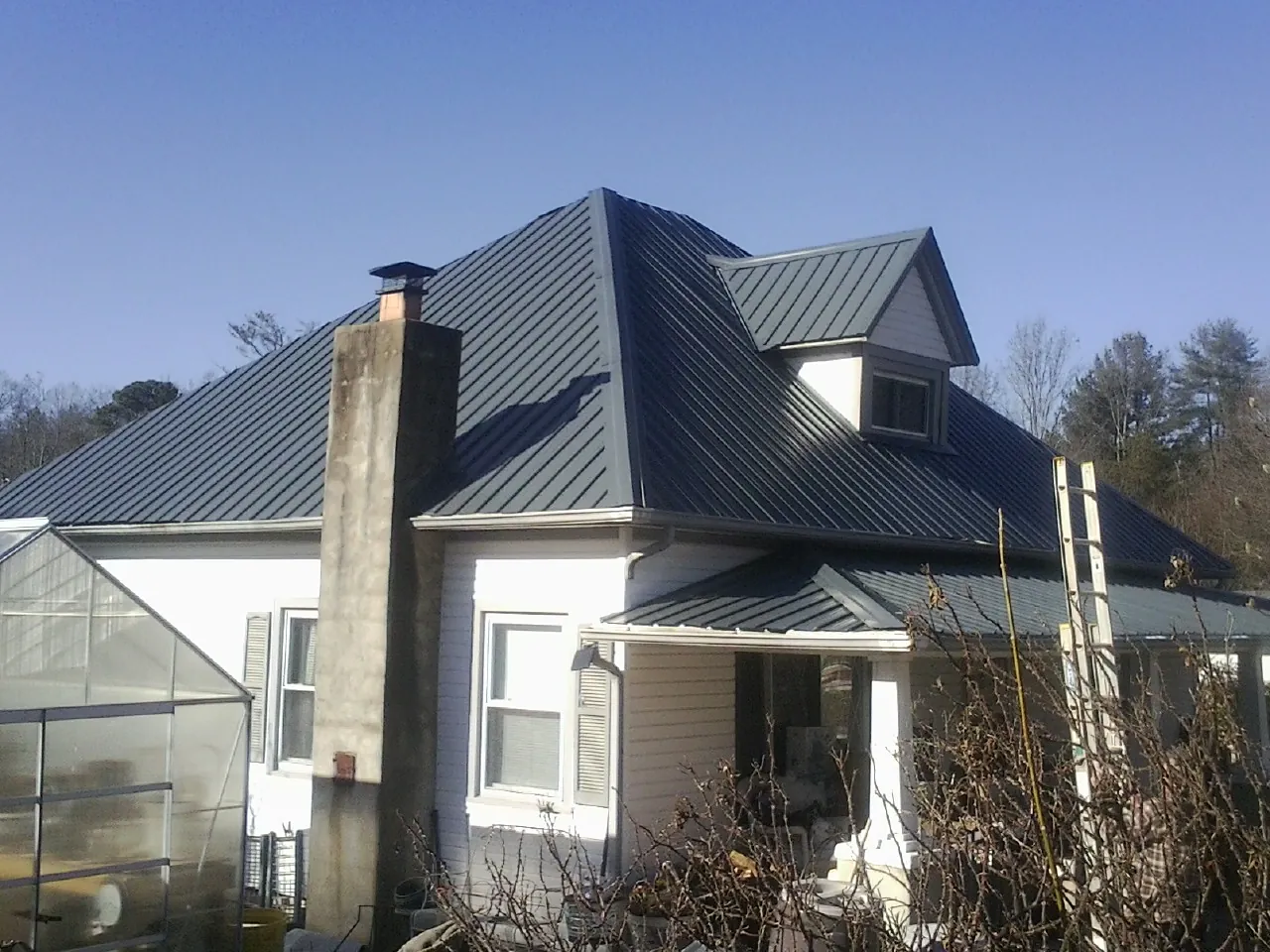 Dark blue standing seam metal roof on a white farmhouse with dormer — Slate & Tile Roof Repair by Roofing Brothers in Holy Cross