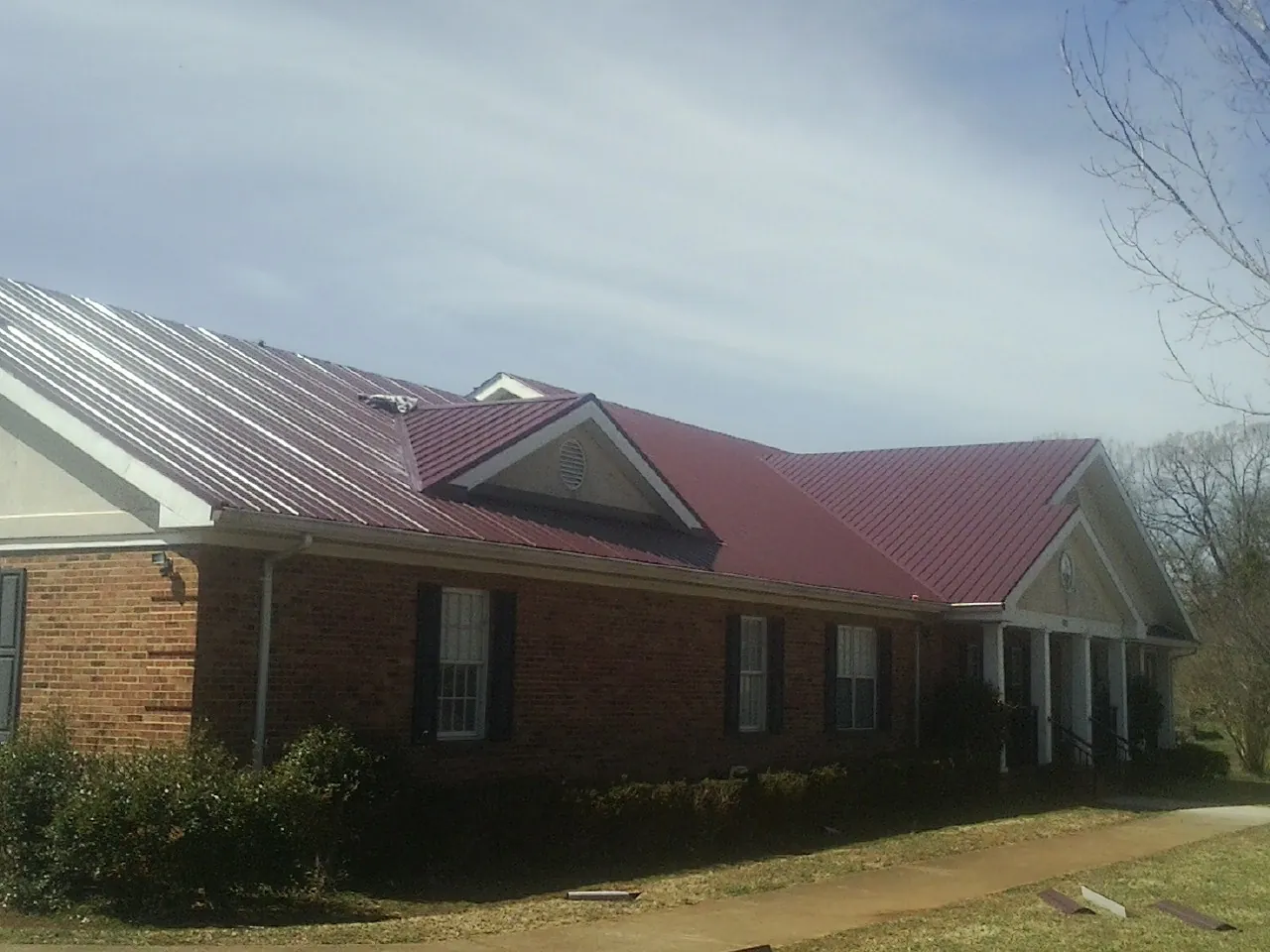 Red metal roof with gabled entries on a long brick building, from a Hail Damage Roof Repair job in Holy Cross