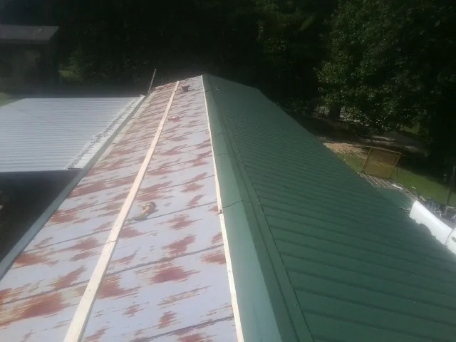 Old rusted panels beside newly installed green metal roofing — Wind Damage Roof Repair by Roofing Brothers in Holy Cross