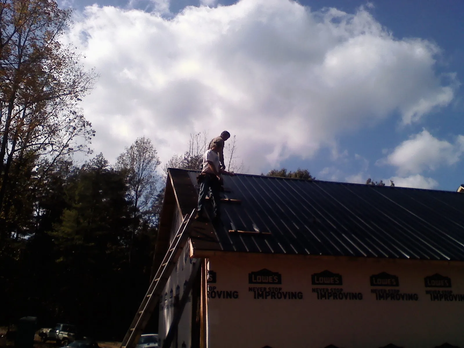 Roofer fastening dark metal panels high against a cloudy sky, from a Roof Inspection job in Holy Cross