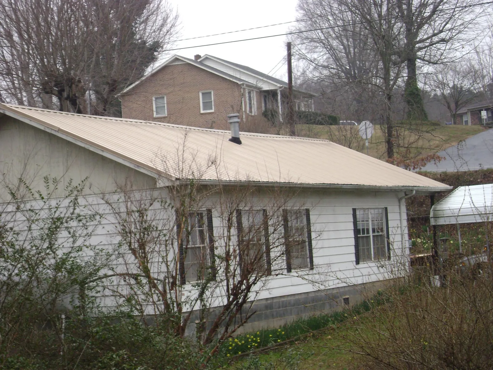 Tan metal roof on a white sided house set into a hillside — Commercial Roofing by Roofing Brothers in Holy Cross