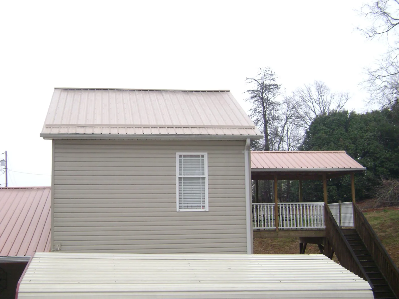 Tan metal roofs on a two story addition and attached porch, from a Roof Replacement job in Holy Cross