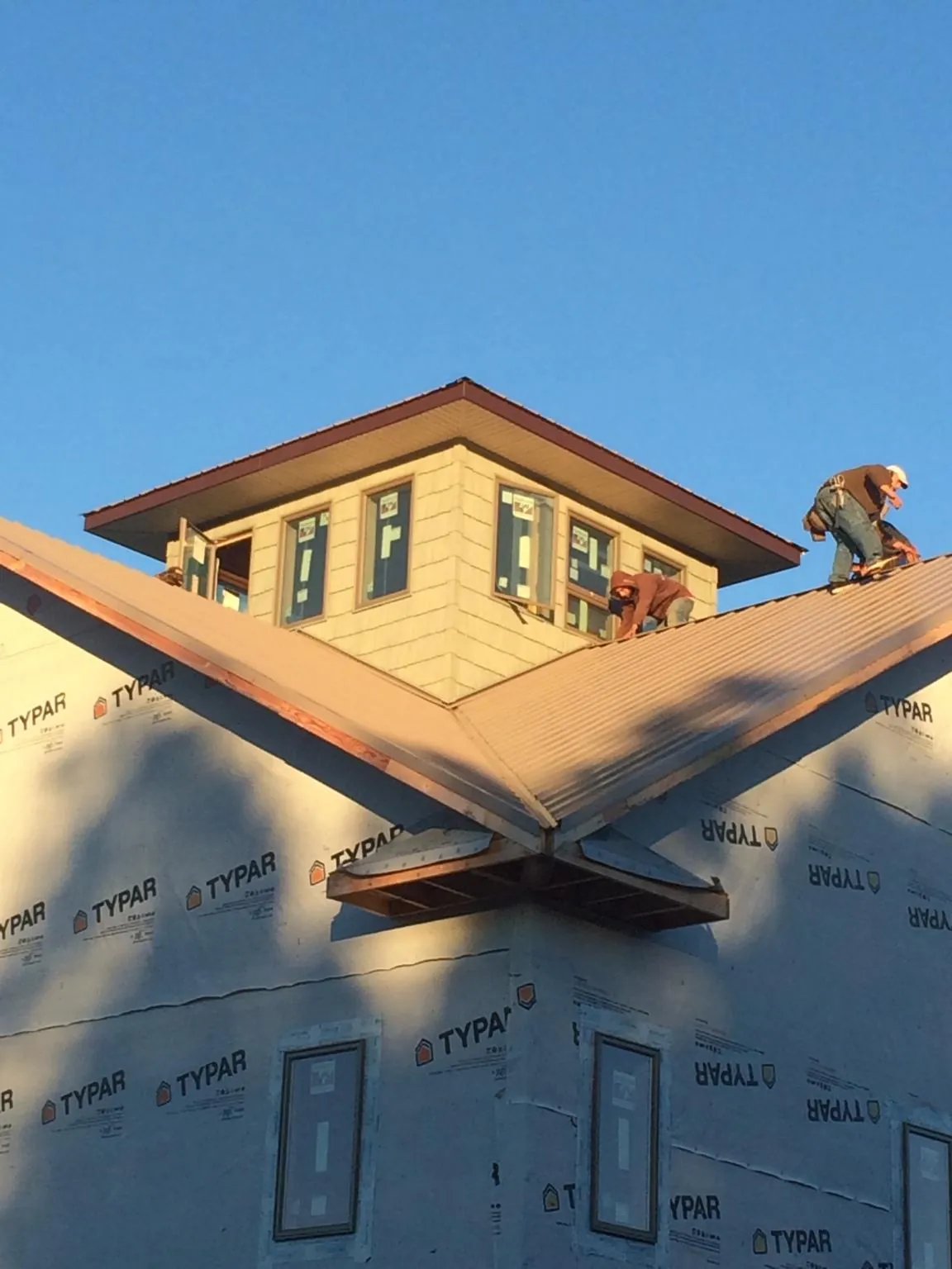 Roofers working around a rooftop cupola on a new metal roof at sunset — Roof Waterproofing in Holy Cross by Roofing Brothers